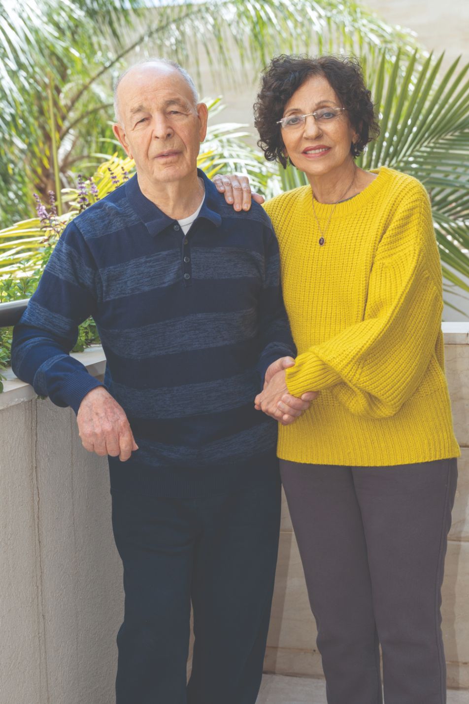 אביבה ואריה פאר זוג מבוגרים עומדים במרפסת מחזיקים ידיים ומחייכים
