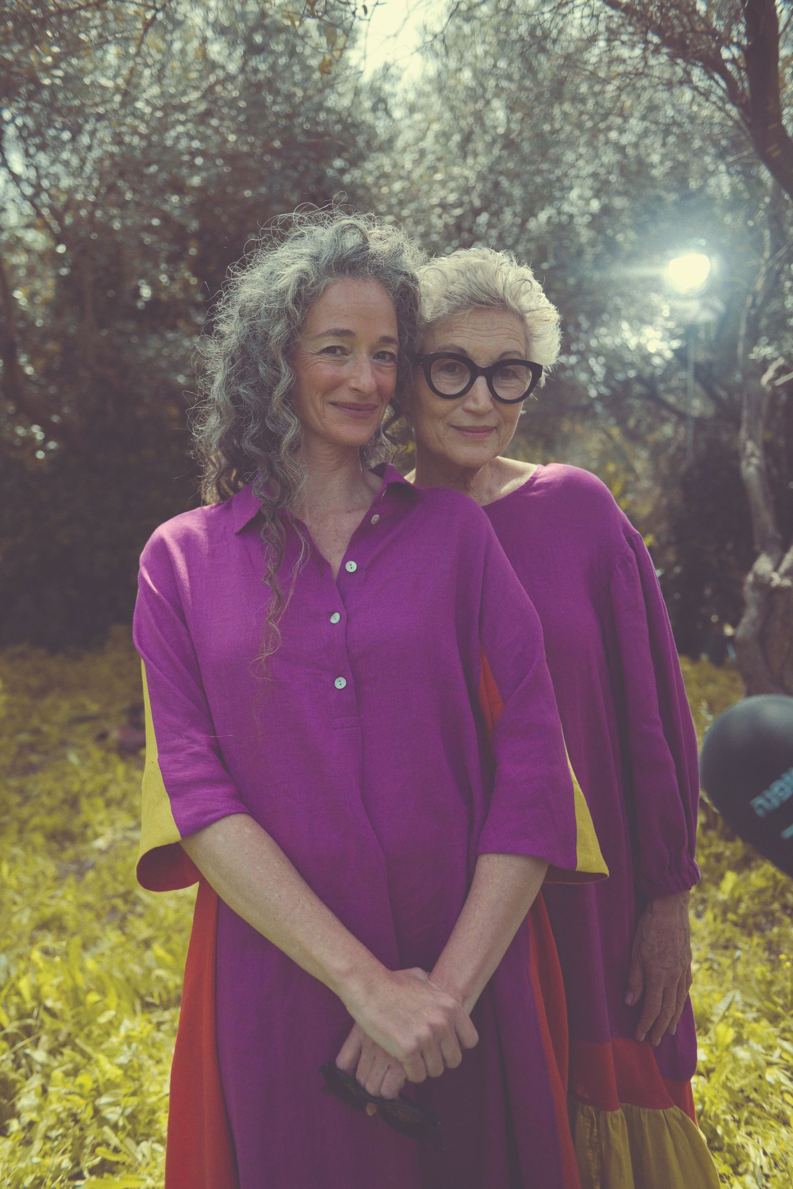 שתי בחורות מבוגרות בגיל השלישי לבושות בסגול נמצאות בטבע ומחייכות 